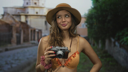 Woman in bikini holding camera in an old town setting, showcasing a youthful tourist exploring...