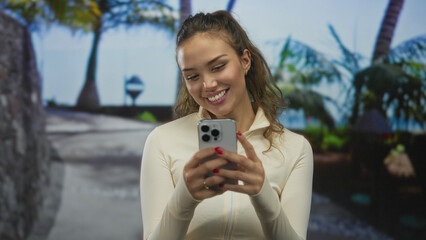 Woman smiling outdoors using smartphone surrounded by tropical scenery captured in daylight...