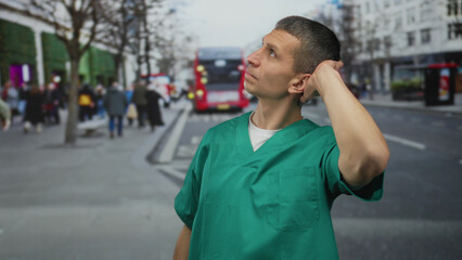 Man wearing green medical uniform standing on a busy street with a background of people and a red...