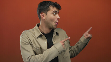 Man lifts finger while pointing at camera over background and male hispanic young figure in orange...
