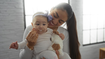 Woman holding baby girl in cozy living room, displaying love and happiness with toy, pacifier, and...