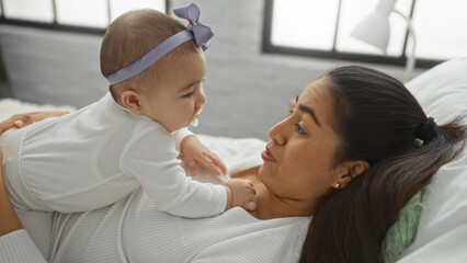 Obraz premium Mother and daughter sharing a loving moment on bed in cozy home environment, highlighting family bond in interior domestic setting with girl and woman interacting indoors.