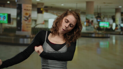 Young woman dancing joyfully in an indoor airport terminal with vibrant surroundings, reflecting a cheerful travel atmosphere.