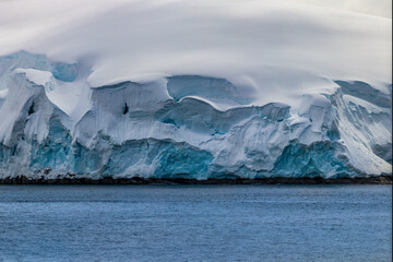 Shoreline of the Antarctic peninsula covered in deep snow. Ocean in foreground. 
