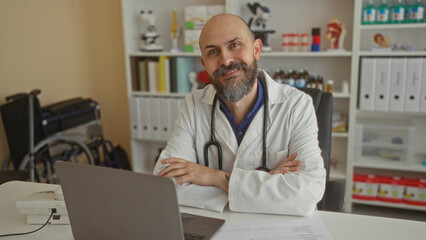 Doctor relaxed in clinic office with arms crossed, sitting at desk with laptop, surrounded by...