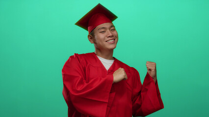 Young chinese man in red graduation attire celebrating against a green background, showcasing a...