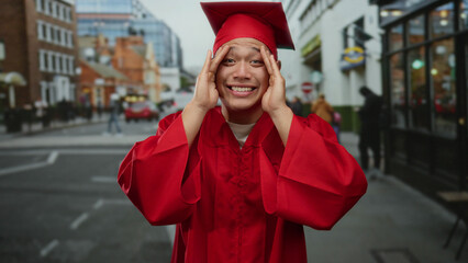 Graduate student in red gown on an urban street displays a range of emotions during a celebratory...
