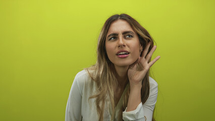 Young blond woman cups hand to ear and taps an invisible door in a photo studio; attention focus...