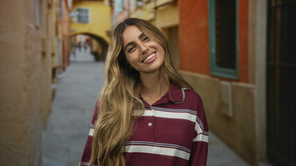Blonde woman places hand on chest and smiles in sunlit cobblestone alley; gratitude warmth...