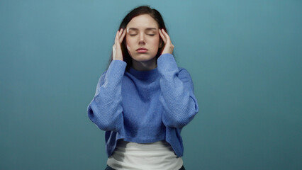 Woman with brunette hair feeling stressed in front of a blue background struggles with headache...