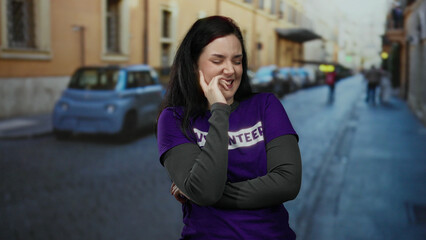 Woman smiling in purple volunteer shirt stands laughing on urban street with blurred cars and...