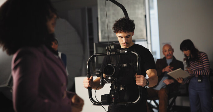 Man, cameraman and stabilizer with journalist on set of broadcast, production process and record. People, tech and cinematographer for shooting news, documentary footage and rehearsal for commercial - Powered by Adobe