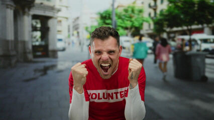 Young man wearing volunteer shirt celebrating success with joy in urban street environment showing...