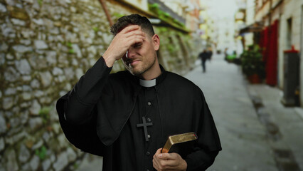 Priest standing on urban street holding bible looking contemplative with buildings in background...