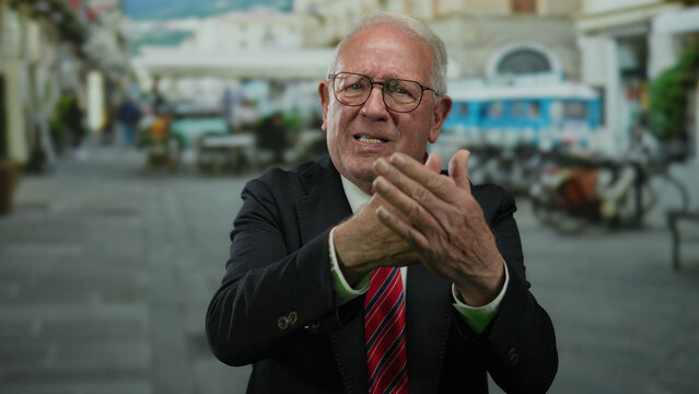 Senior man in business suit gesturing passionately on a busy outdoor street with blurred buildings and a vibrant urban background.