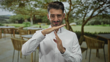 Young smiling man in white shirt making time out gesture with hands in building; pause calm focus...