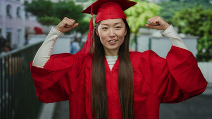 Confident woman in red graduation gown poses triumphantly on urban street, symbolizing success and...
