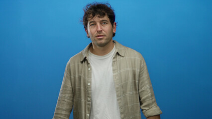 Man in casual shirt stands against blue background expressing emotion with hands raised, capturing...