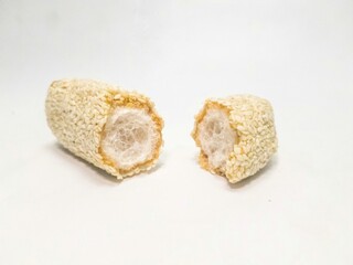 A close-up of a sesame-covered cookie (manco) cut in half, revealing its airy, hollow interior. A crispy, traditional Indonesian snack on a white background.