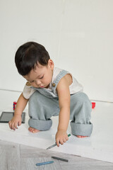 a baby sitting on the floor, holding a pencil and surrounded by various objects. In the background,...