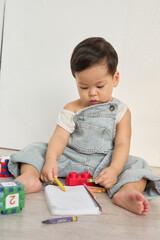 a baby sitting on the floor, surrounded by a variety of toys, including a book, crayons, and a toy...