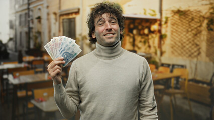 Hispanic man holding polish zloty banknotes on a city street terrace with outdoor restaurant...