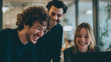 Three young professionals collaborate happily around a laptop in a modern office setting.