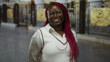 Woman with braids smiling on city street in daytime wearing glasses and sweater showing vibrant...