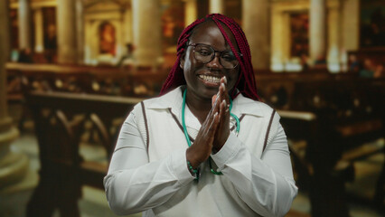 African american woman clapping and smiling indoors in a church setting, wearing glasses and a...