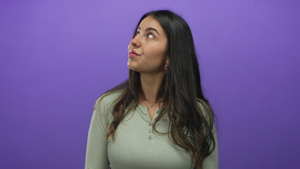 Woman with long dark hair stands against an isolated purple background, wearing casual attire, embodying a youthful hispanic appearance.