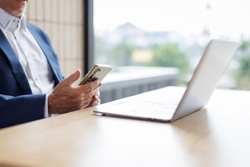 Portrait of a cheerful mid adult businessman using phone for investment plan chatting contact Investor searching for informationat at workplace office. connecting people concept