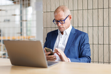 Portrait of a cheerful mid adult businessman using phone for investment plan chatting contact...