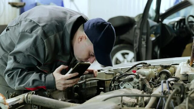 Professional mechanic carefully checking vehicle engine, using smartphone for diagnostic imaging within high tech automotive workshop environment - Powered by Adobe