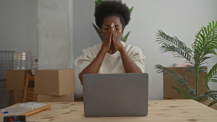 Woman stressed sitting at a desk with laptop in a new home living room surrounded by cardboard...
