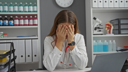 Woman stressed at her clinic workstation, covering face with hands while sitting at desk with...