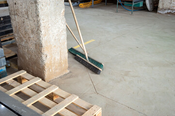 Broom and dustpan positioned beside a concrete pillar on the floor of a spacious warehouse, indicating ongoing cleaning efforts