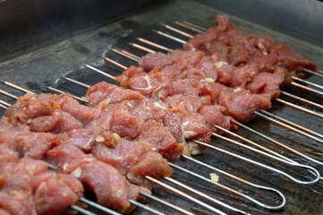 Chunks of marinated meat are arranged on skewers and grilling over hot coals, filling the air with...