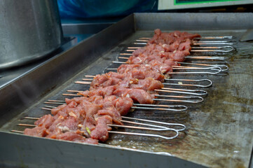 Marinated meat skewers are placed on a grill, releasing savory aromas at a bustling evening market...