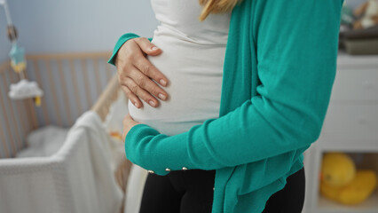 Obraz premium Woman cradling pregnant belly indoors, standing in a softly lit bedroom beside a wooden crib, symbolizing motherhood in a peaceful home setting.
