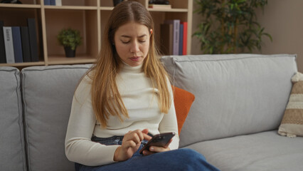 Woman relaxing on a comfortable sofa in a modern living room while using a smartphone, showcasing a peaceful indoor home atmosphere with natural light and elegant decor.