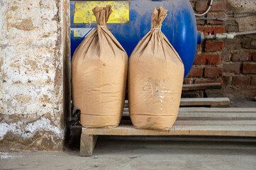 Two large bags filled with materials rest on a wooden platform in a warehouse, with sunlight...