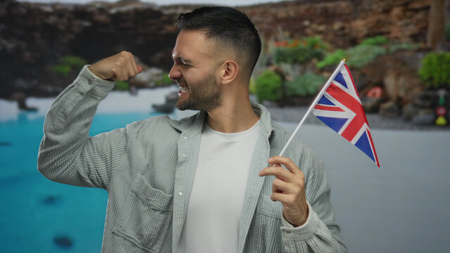 Hispanic man in a hotel swimming pool confidently flexing his arm while holding a uk flag, symbolizing joy and patriotism.