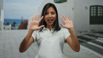 Woman gesturing on sunny street with bright blue ocean backdrop, cheerful vibe and casual attire...