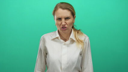 Woman expressing dislike with grimace in white shirt against green backdrop isolated background...