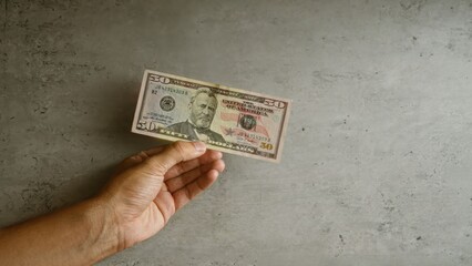 Hand holding fifty-dollar bill against concrete background, featuring american currency with...