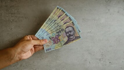 Woman holding multiple romanian lei banknotes against a concrete background, showcasing local...
