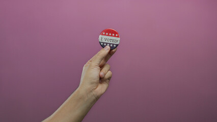 Caucasian man holds a voting badge against an isolated pink background, symbolizing civic...