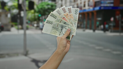 Caucasian man holding czech koruna banknotes on a city street, emphasizing money and outdoor urban...