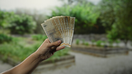 Man holding danish krone banknotes in a garden setting, illustrating the concept of finance and...