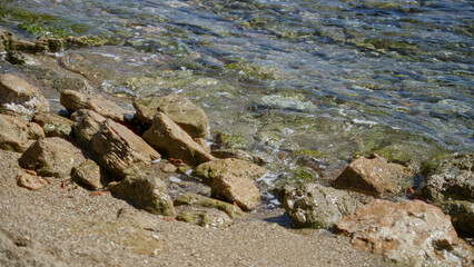 Mediterranean shoreline with rocks and clear sea water glistening under the sunny blue sky, capturing the tranquil beauty of a natural coastal setting.